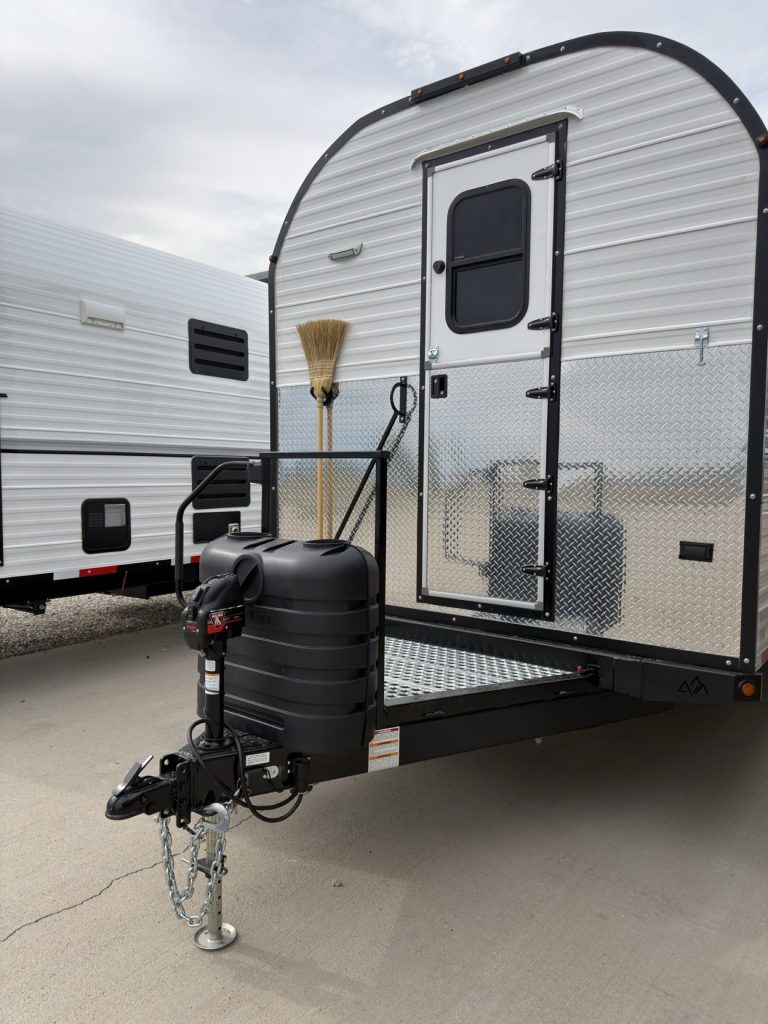 White range camp with Dutch door, fold-up steps, black propane cover, and broom at the front entry.