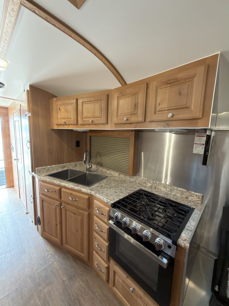 Kitchen wall with hardwood cabinets, double sink, gas range, microwave, and refrigerator.
