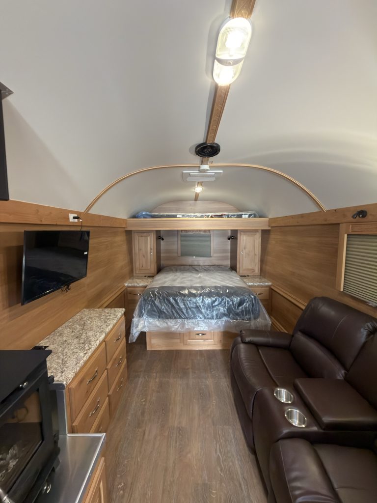 Queen bed at the rear of the living area, flanked by cabinets and a two-person recliner.