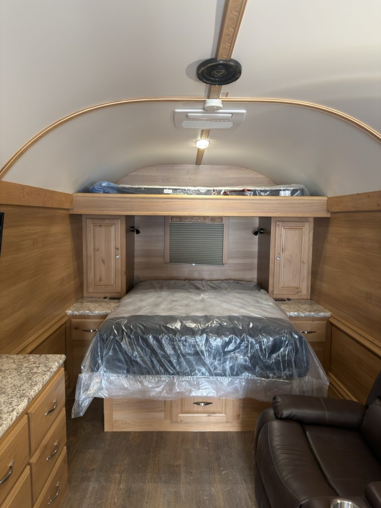 North-south queen bed with nightstands, overhead cabinets, and rear egress window.