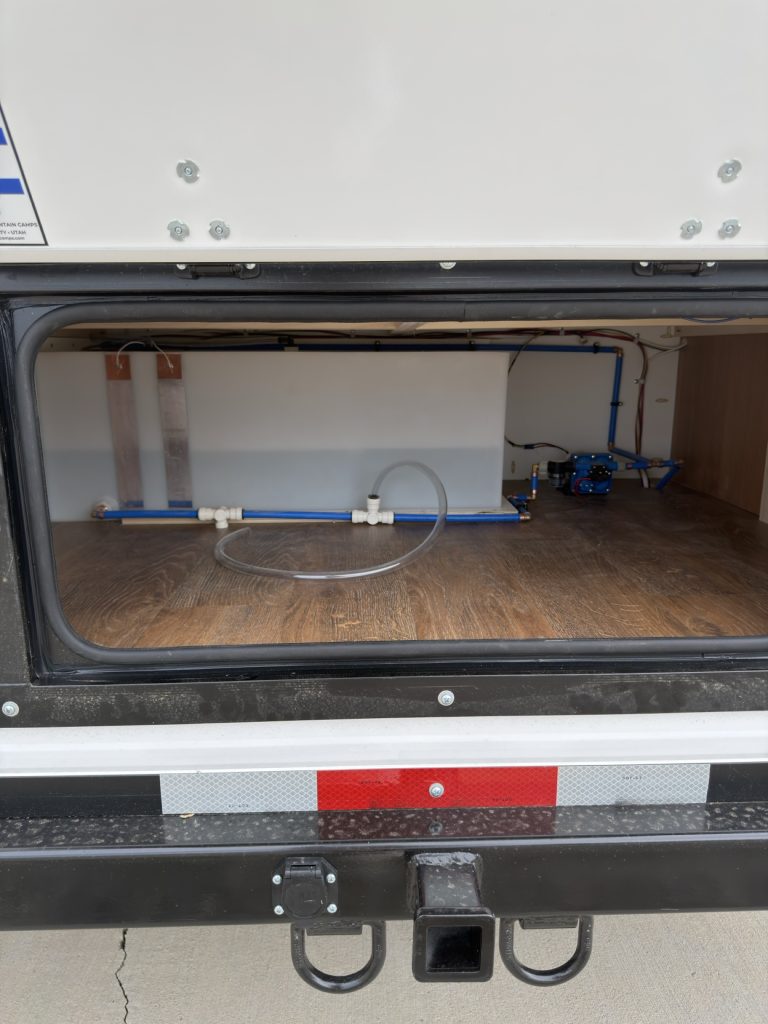 Fresh water tank, plumbing, and open storage inside an exterior compartment.