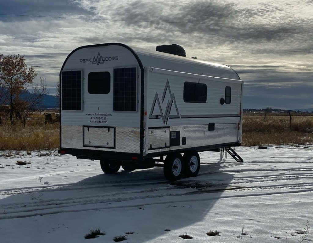 Compact Peak camp trailer parked on snow under a dramatic winter sky