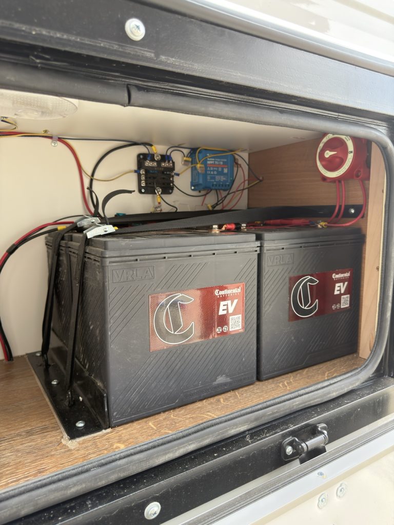 Four AGM batteries with wiring and controller inside an exterior compartment.