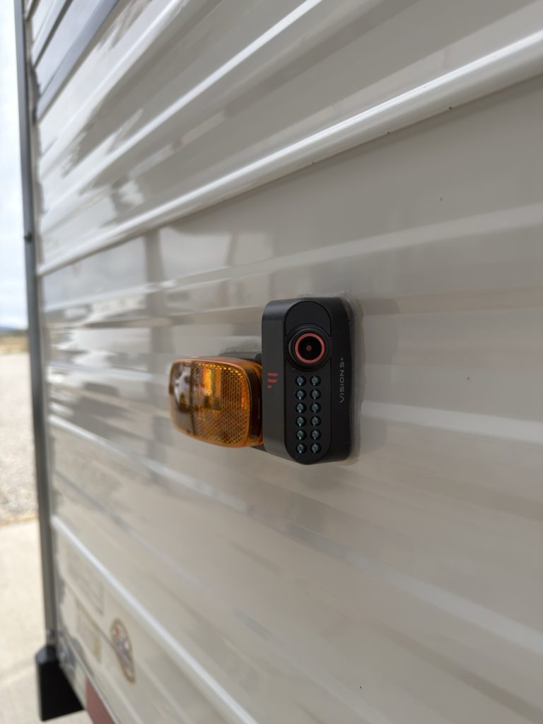 Amber marker light and black side camera mounted on white siding.