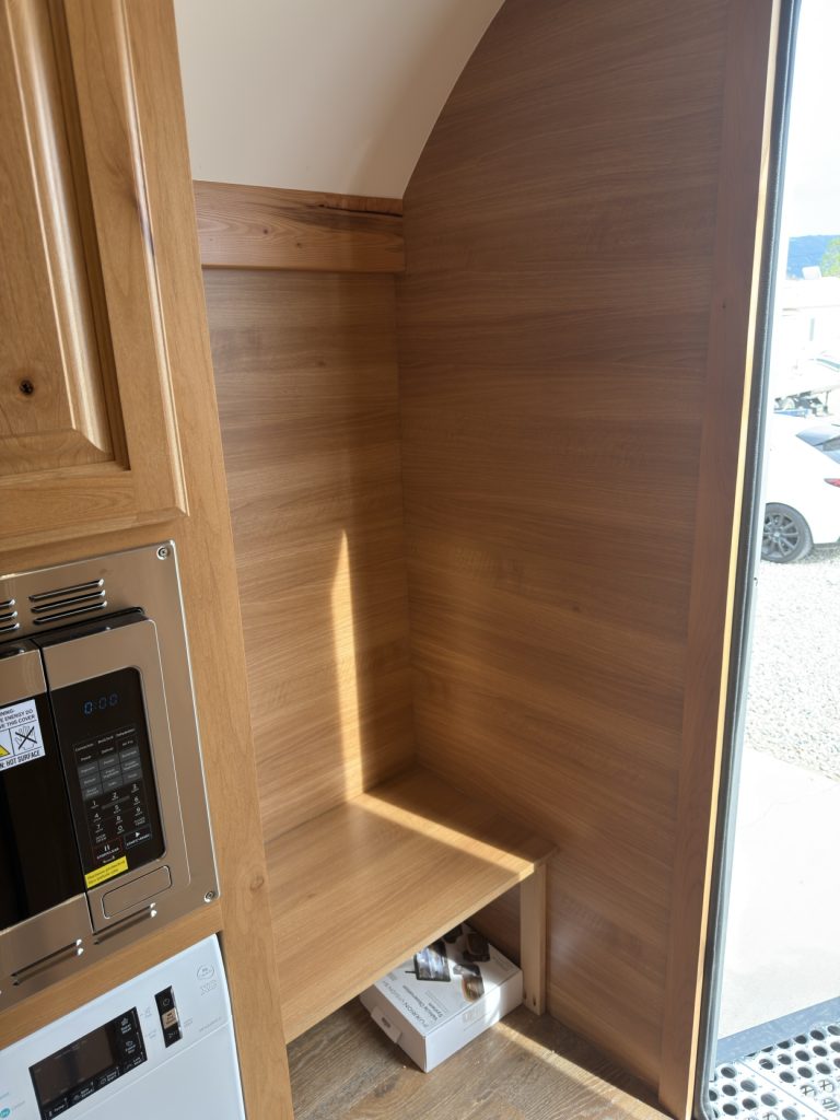 Wood-lined mudroom alcove with bench and open storage beside the microwave.