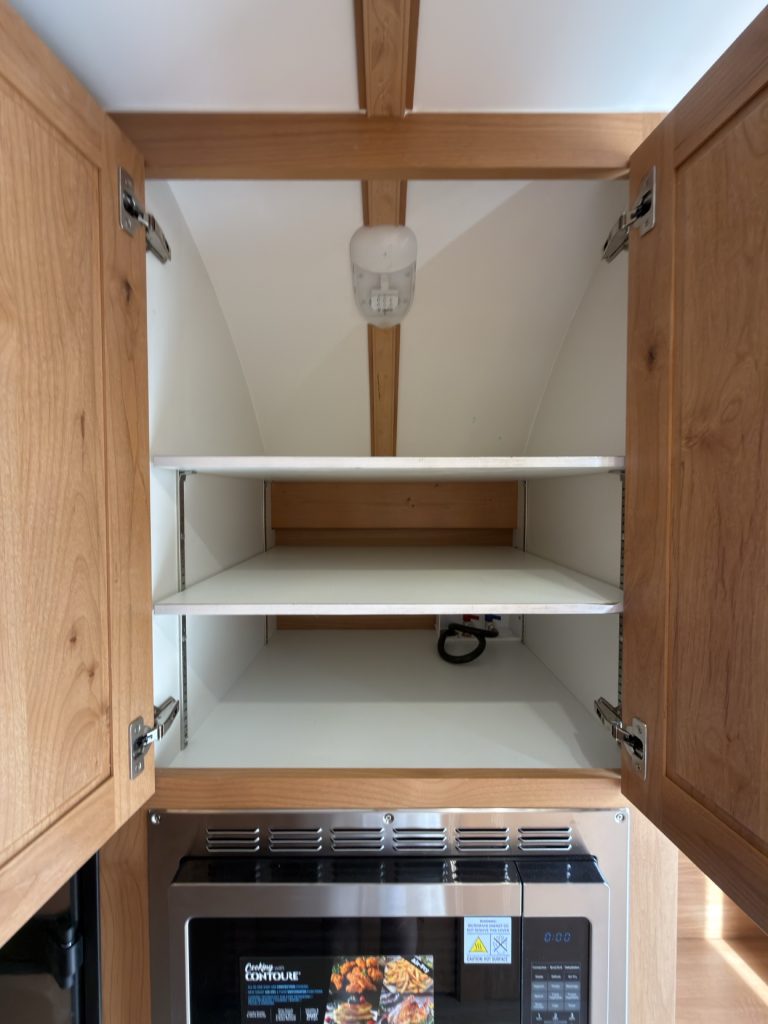 Open double-door storage cabinet above the microwave with adjustable shelves.