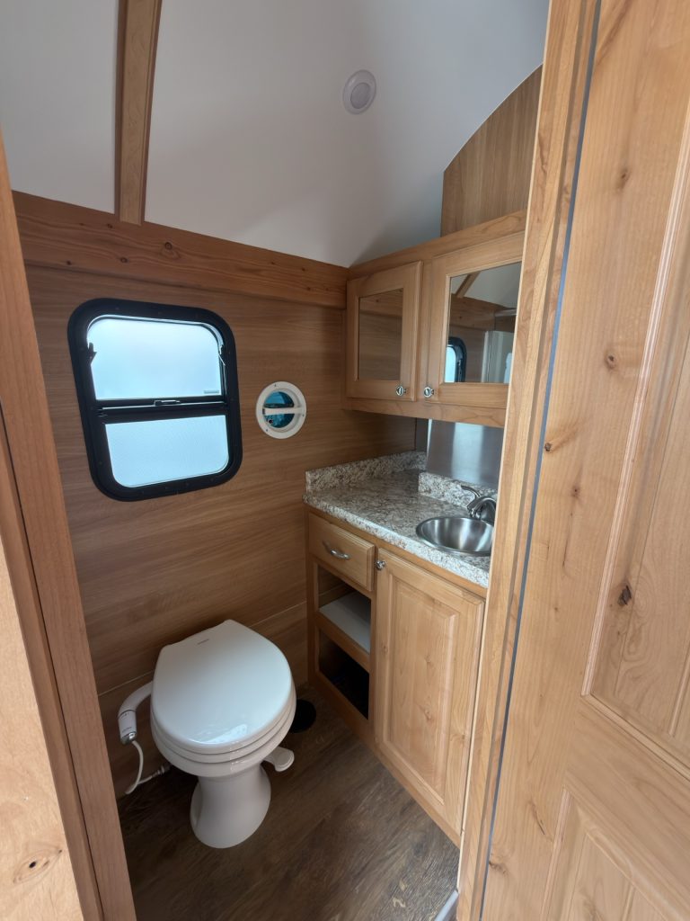 Bathroom interior with porcelain toilet, stainless sink, and open shelving.