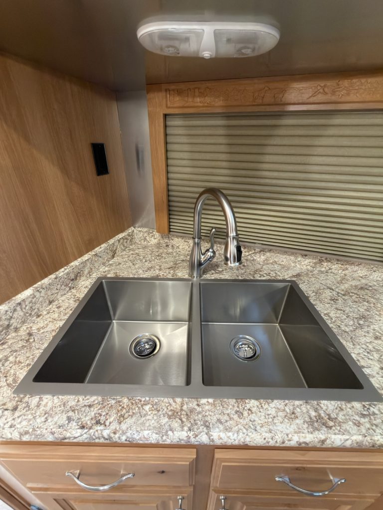 Double stainless steel sink with residential faucet beneath a window shade.
