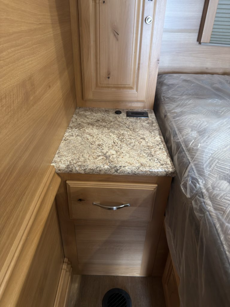 Nightstand with granite-pattern top, drawer, cabinet, outlets, and floor vent beside the bed.
