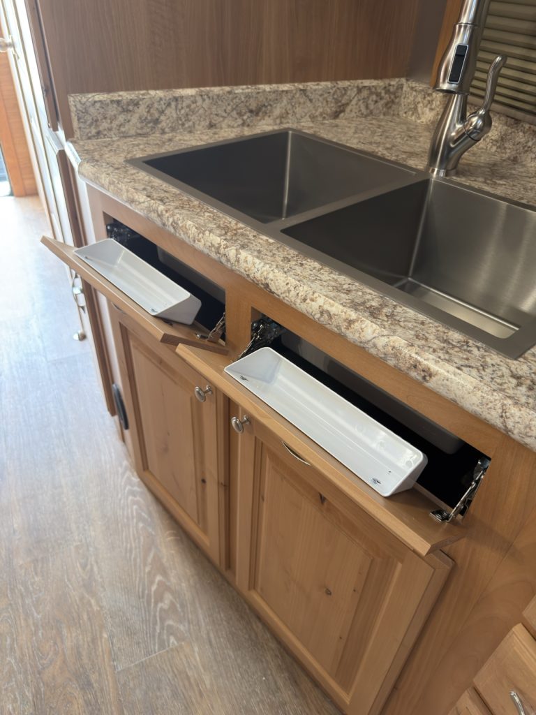 Double sink cabinet open with two white tip-out trays.