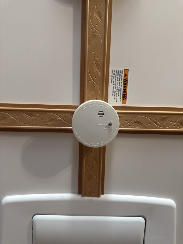 White smoke detector mounted on carved rosewood ceiling trim.