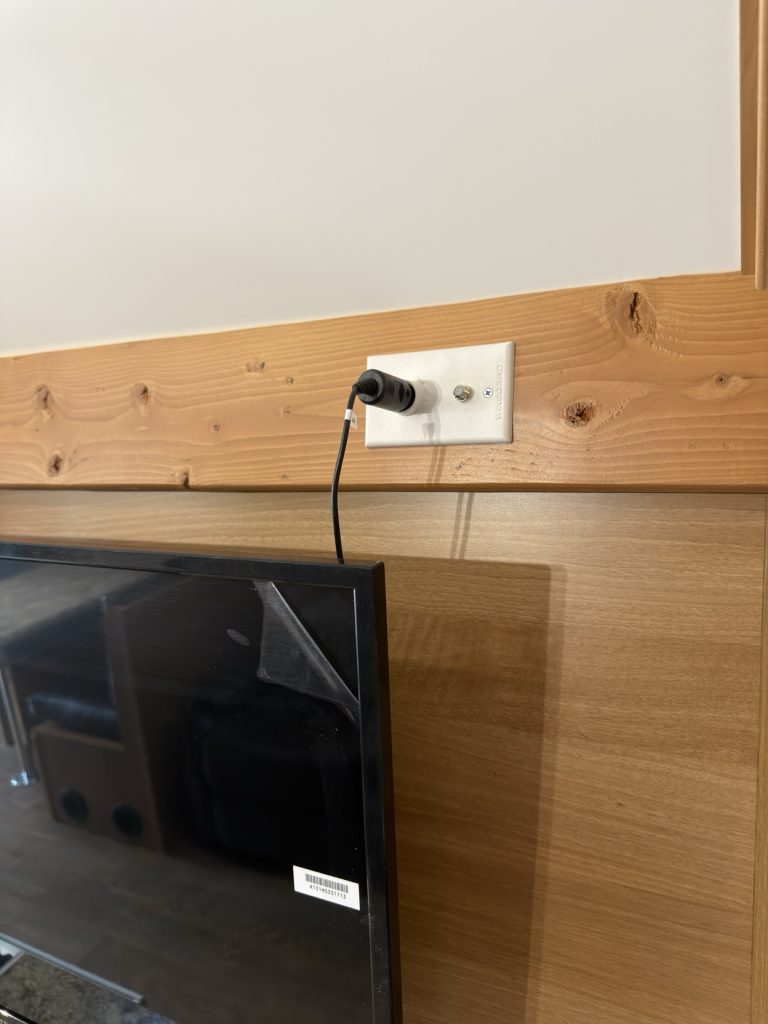 Flat-screen television beside a white power outlet on the wood wall.