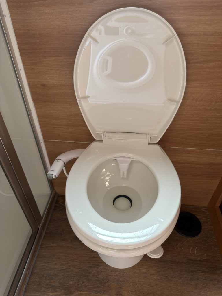 White porcelain toilet with foot-flush pedal and bidet attachment.
