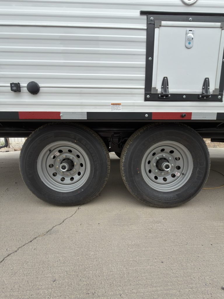 Tandem steel wheels with 8-lug hubs beneath an exterior storage door.