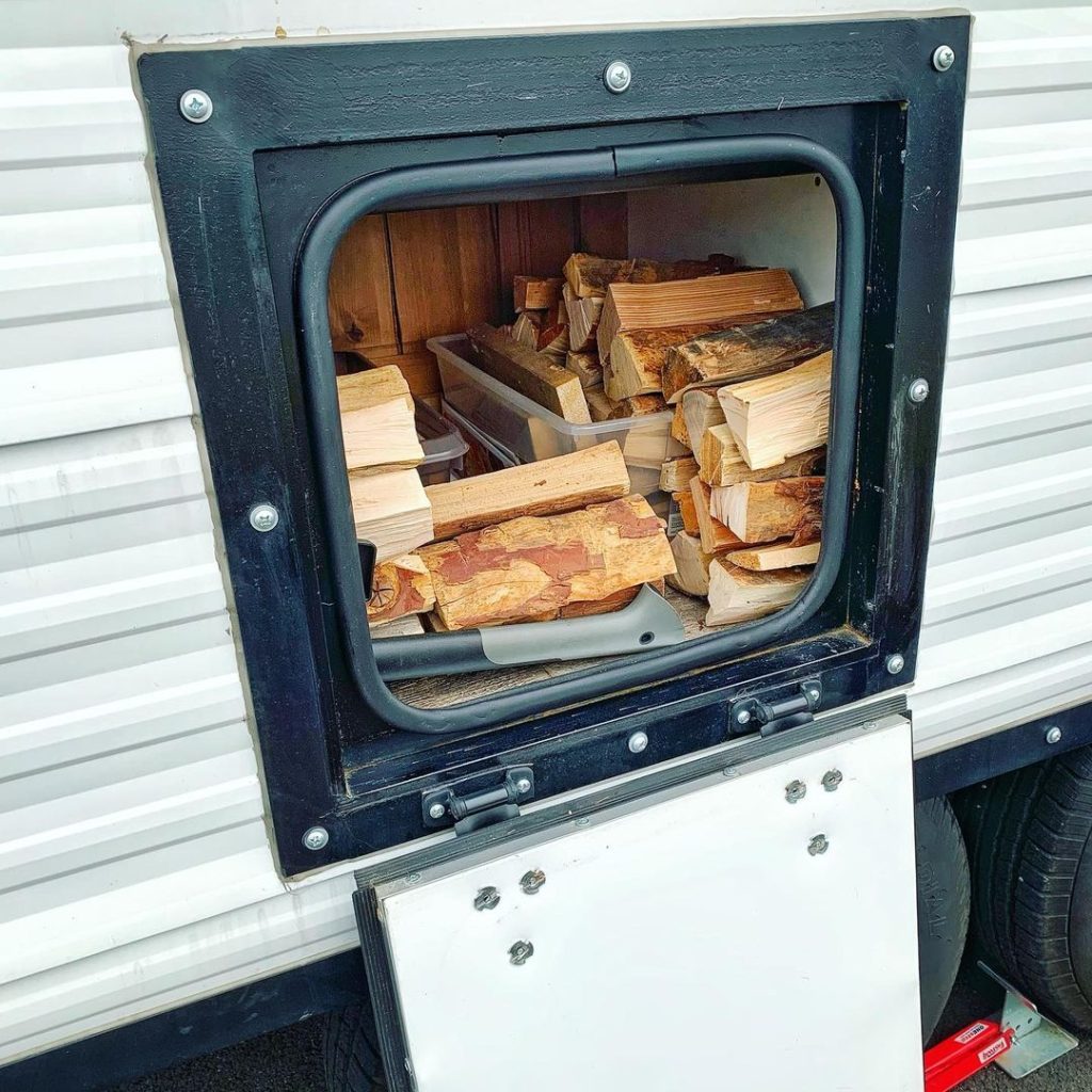 Open exterior storage compartment filled with split firewood on a Peak camp trailer