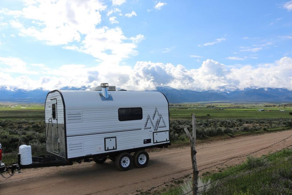 Peak camp trailer parked above a broad mountain valley beneath blue skies