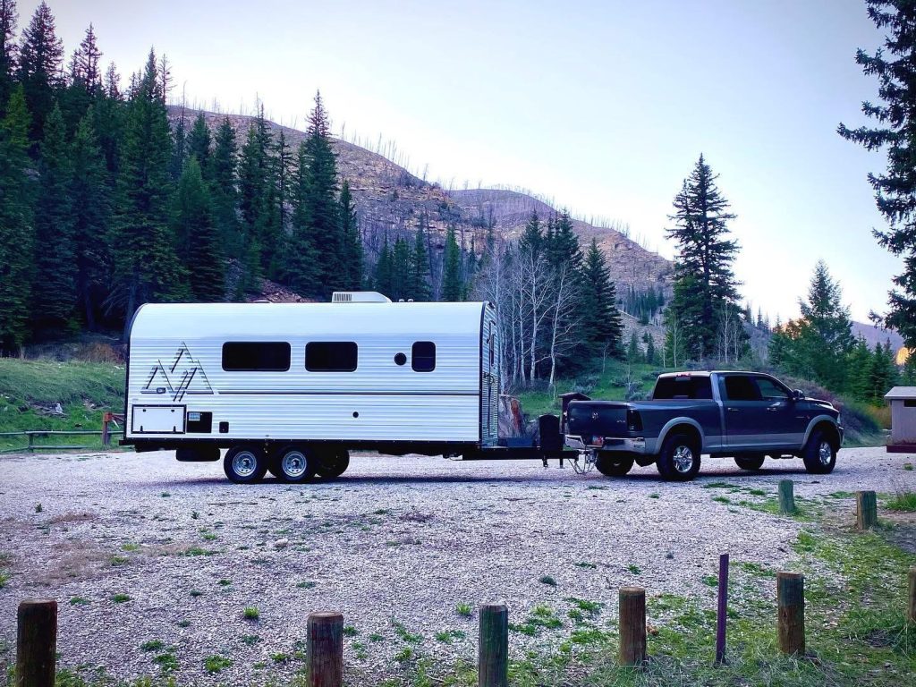 Peak camp trailer and tow vehicle at a forested mountain campsite