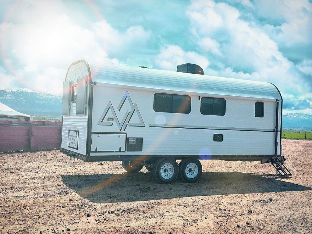 Peak camp trailer set up on a gravel campsite beneath bright clouds