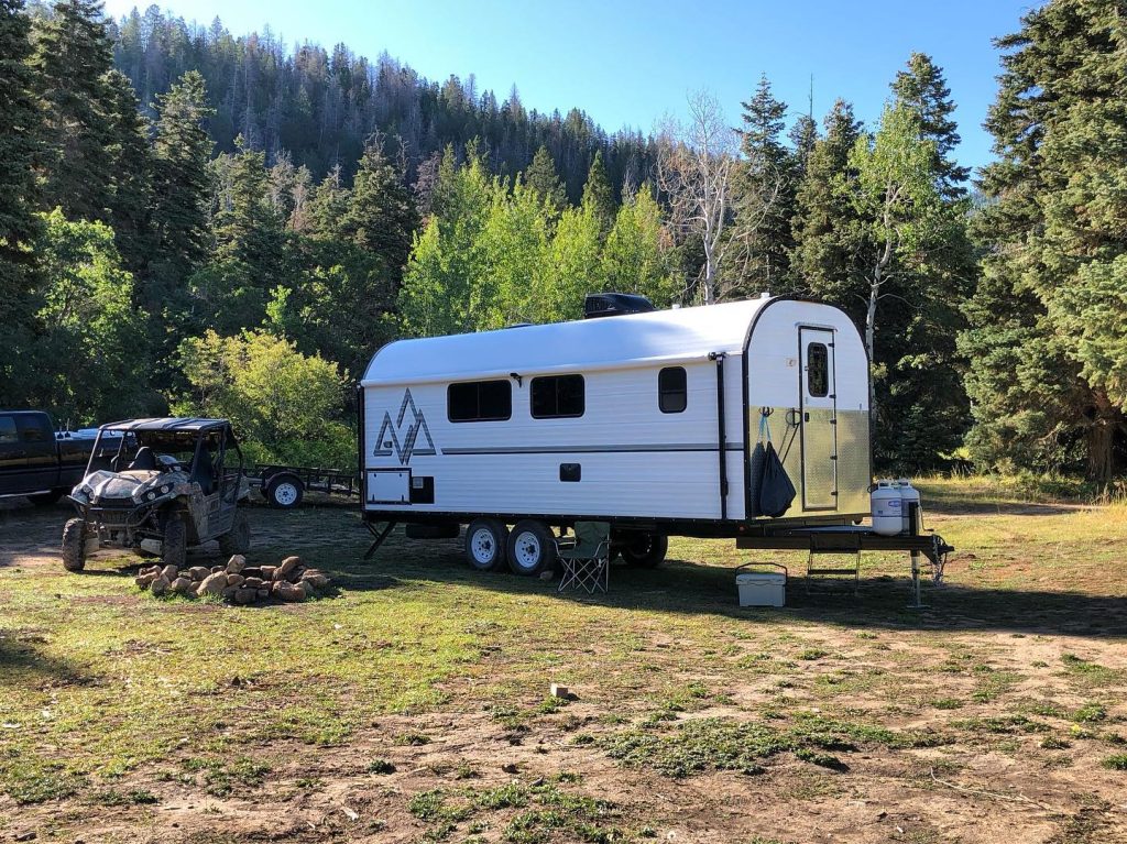Peak camp trailer set up with outdoor equipment at a forest mountain basecamp