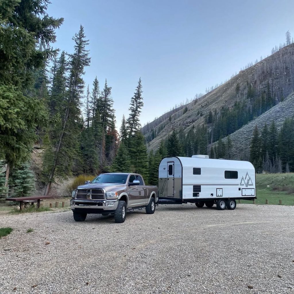 Pickup and Peak camp trailer parked beside a forested mountain trailhead