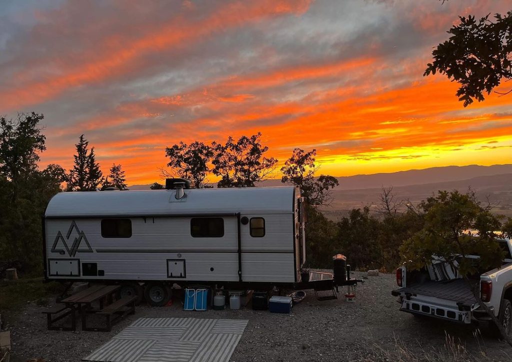 Peak camp trailer at a campsite beneath a dramatic red and orange sunset