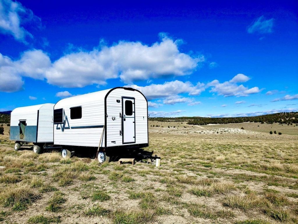 Peak camp trailer set up on open rangeland beneath vivid blue skies