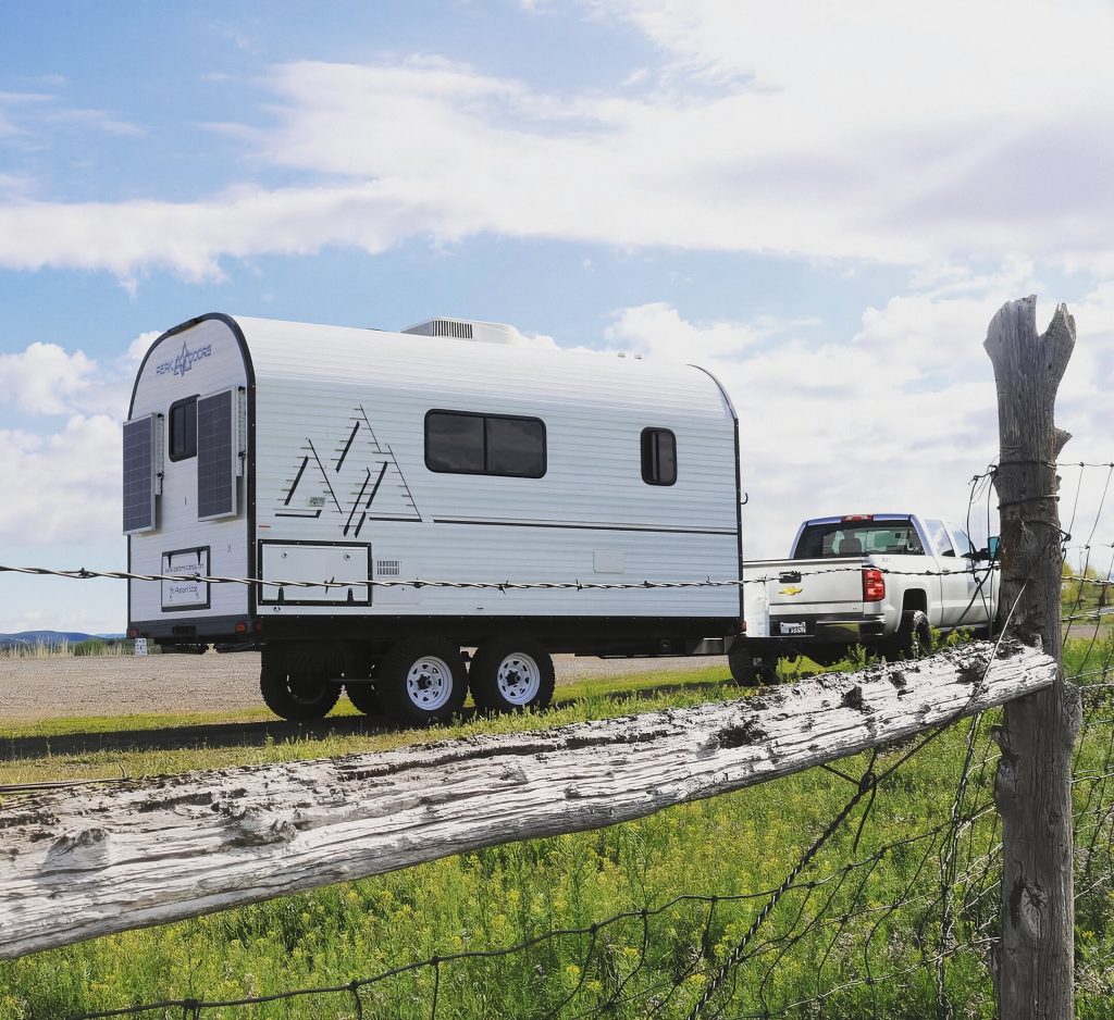 White Peak camp trailer beside a rustic split-rail fence under a bright sky