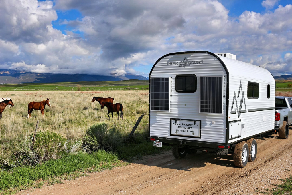 Rear view of a Peak camp trailer parked near horses grazing in open country