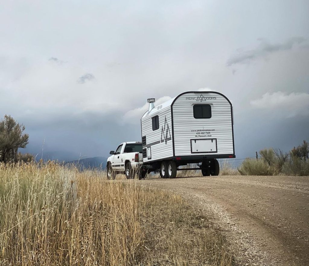 Pickup and Peak camp trailer parked beside tall high-desert grasses and distant hills