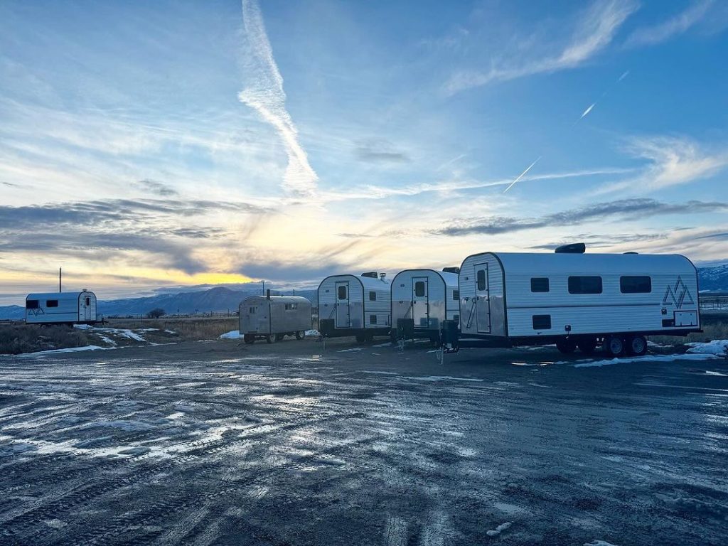 Multiple Peak camp trailers parked together outside the workshop beneath evening clouds