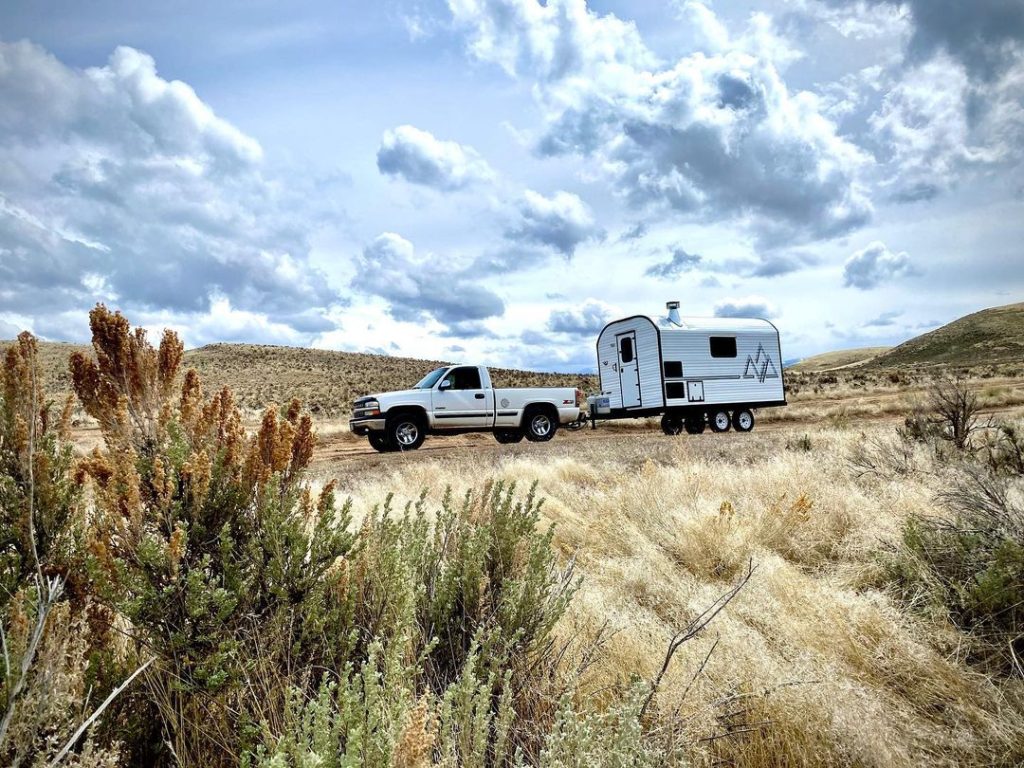 Pickup towing a compact Peak camp trailer across open sagebrush country