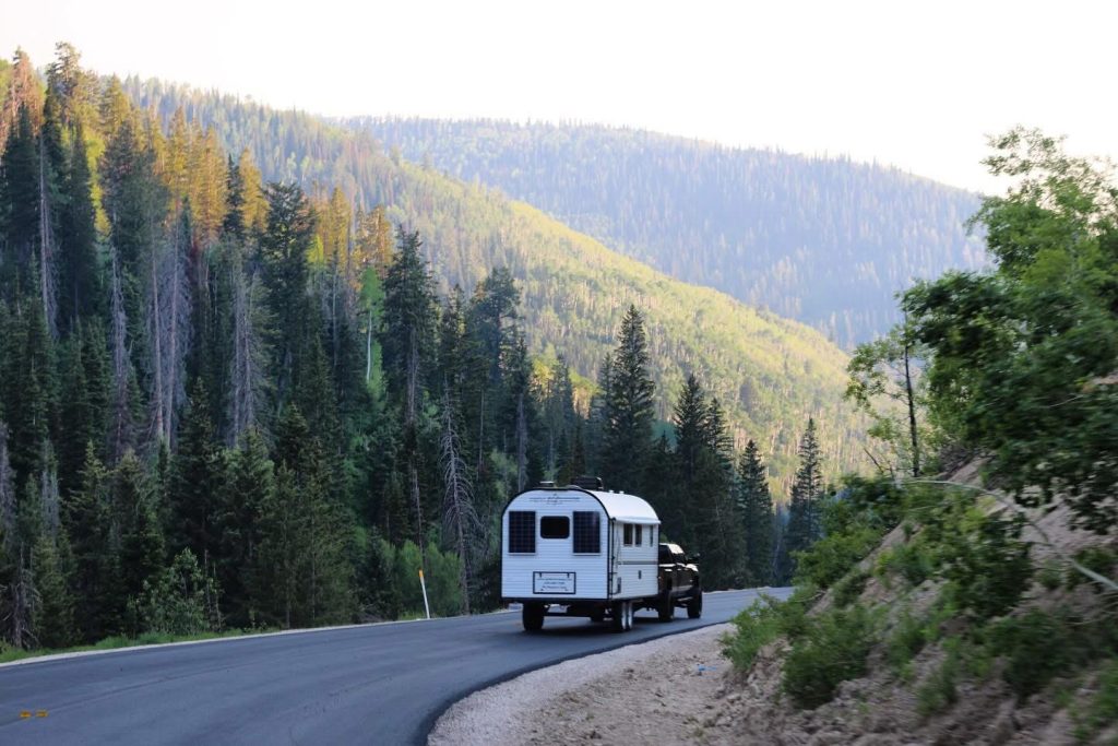 Rear view of a Peak camp trailer traveling down a winding forest mountain road
