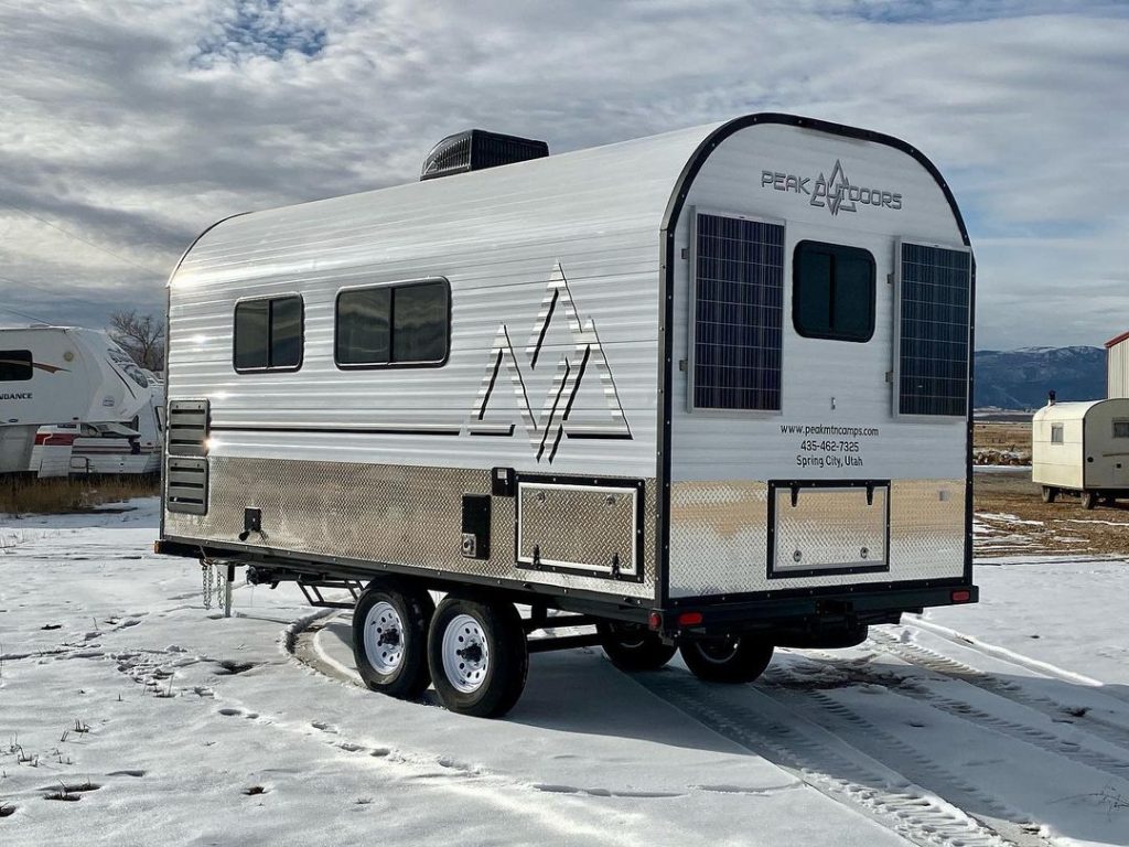 Custom Peak camp trailer displayed on fresh snow beneath winter skies
