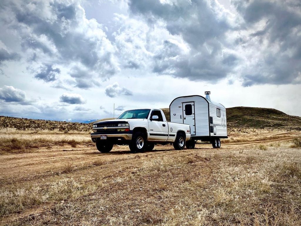 Pickup towing a compact Peak camp trailer along a remote dirt road