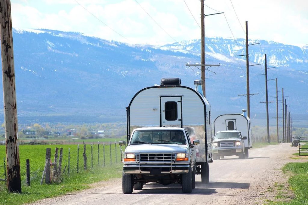 Pickup towing a Peak camp trailer along a rural highway with mountains in the distance
