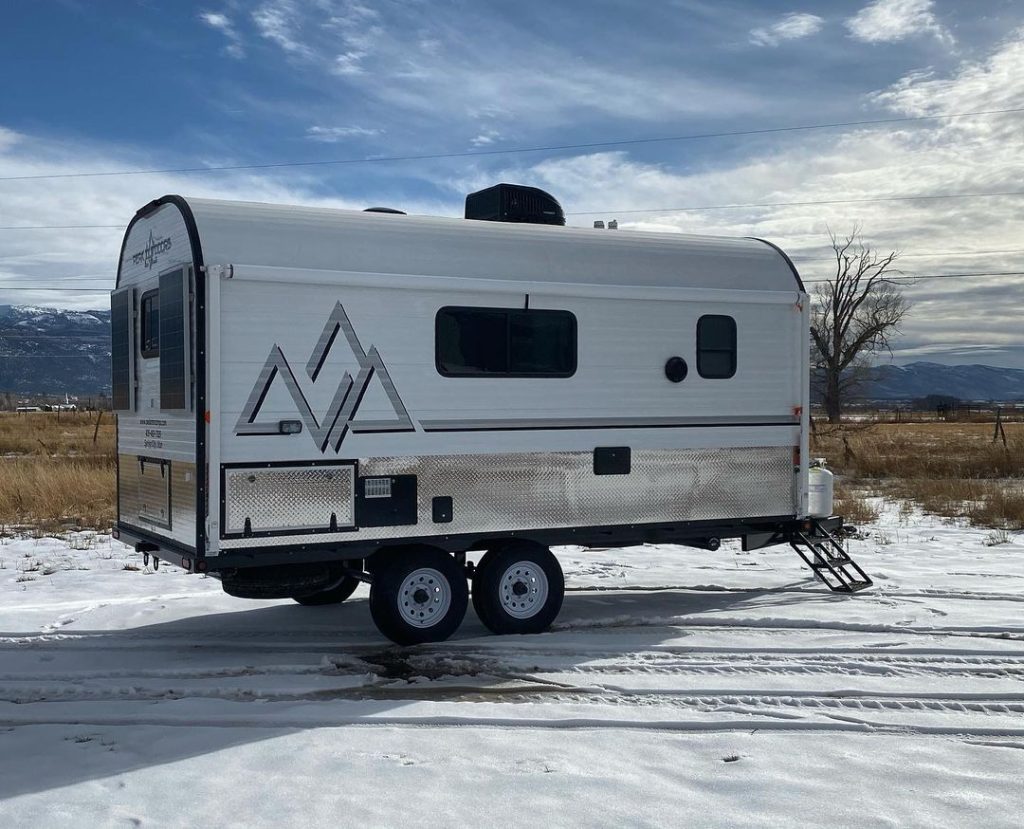 Peak camp trailer parked on snow with mountain country in the background