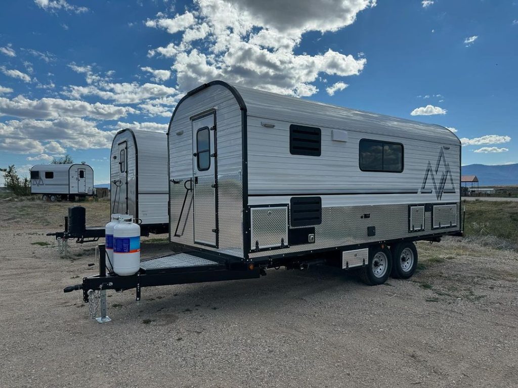 Peak camp trailer set up on gravel near the workshop beneath dramatic clouds