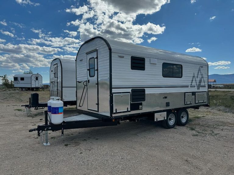 Peak camp trailer set up on gravel near the workshop beneath dramatic clouds