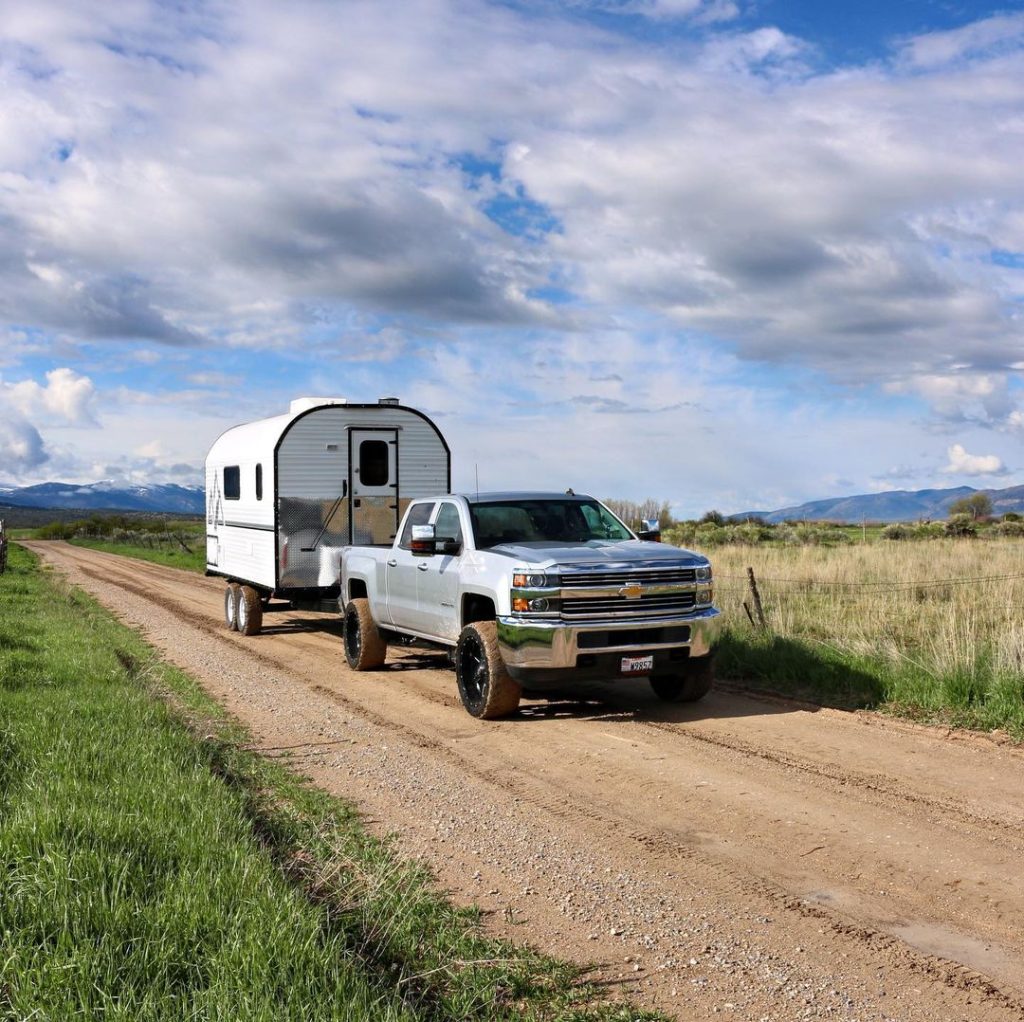 Pickup towing a compact Peak camp trailer along a rural dirt road