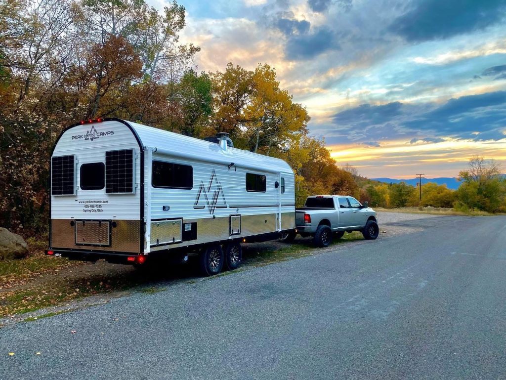 Pickup towing a Peak camp trailer along a mountain road at sunset
