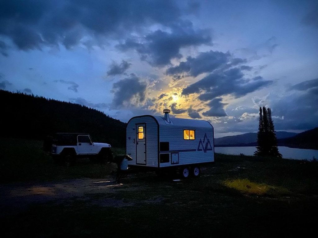 Peak camp trailer at a dark mountain campsite beneath a bright rising moon