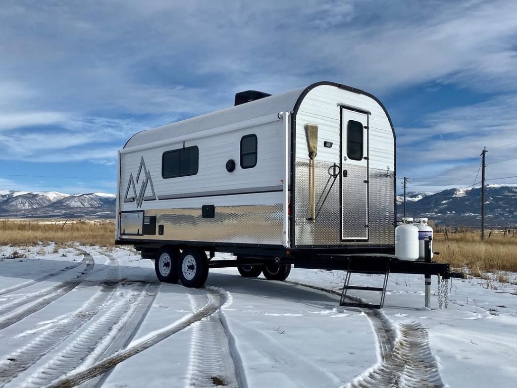 Side and front profile of a Peak camp trailer parked on snow