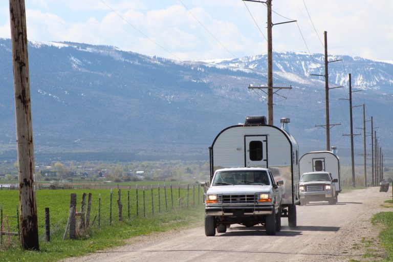 Two Peak Mountain Camps traveling a rural road below snow-covered mountains