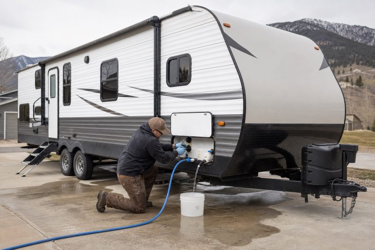 Technician flushing a travel trailer fresh-water system during spring de-winterization