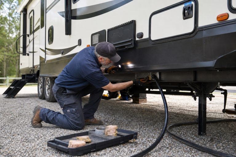 Technician inspecting and sealing a small rodent entry point beneath a travel trailer