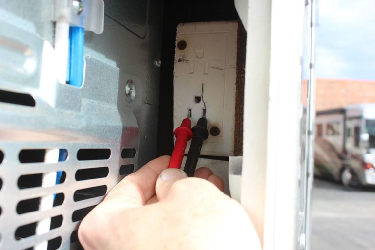 Qualified technician testing the electrical supply behind an RV refrigerator
