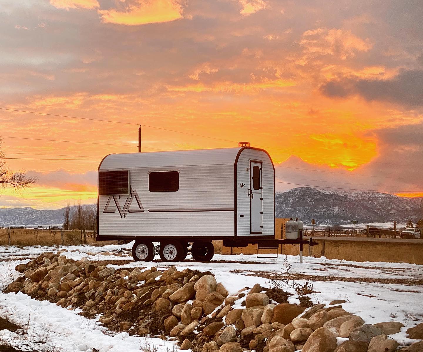 Peak camp trailer parked in snow beneath a winter sunset