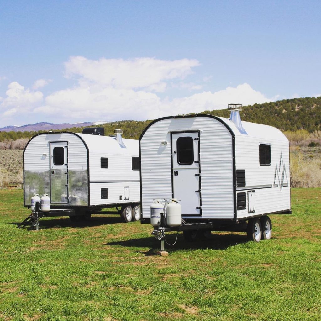 Two custom camp trailers parked side by side on a grassy campsite