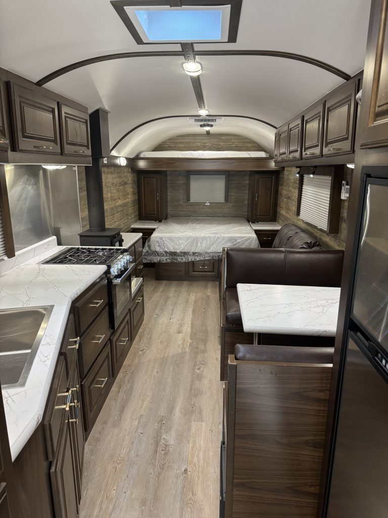 Living and sleeping area inside the untitled X35 camp with recliners, north/south bed, bunk, and wood stove