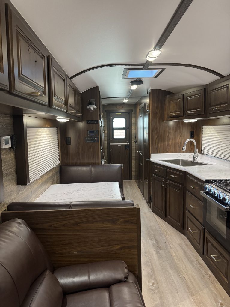 Rear-facing view inside the untitled X35 camp showing the dinette, kitchen, cabinetry, and entry